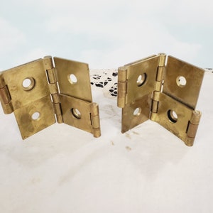 May include: Two brass hinges with four sections each. The hinges are folded and have a shiny, metallic finish.