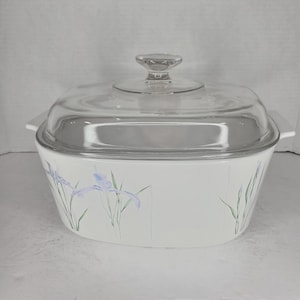 May include: White ceramic casserole dish with a glass lid. The dish has a floral design with blue and green irises.
