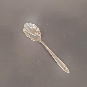 May include: A silver sugar spoon with a scalloped edge and a long, slender handle.