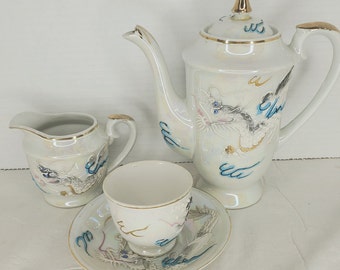Op de afbeelding: Wit porseleinen theeservies met een drakenontwerp. De set bevat een theepot, een roomkan, een kopje en een schoteltje.