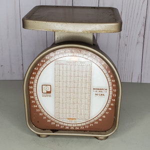 May include: A vintage silver and brown metal scale with a circular dial that reads up to 50 pounds by 2 ounces. The scale is labeled "Monarch Y-Line Model Y-50" and "Pelouze Scale Co.". The dial also includes a chart for parcel post by zones.