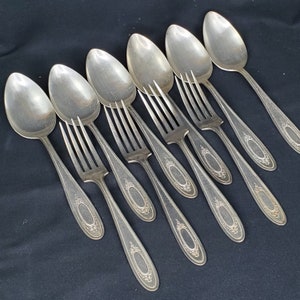 May include: A set of eight silver-plated forks and spoons with ornate handles. The cutlery has a vintage look and is arranged in a row on a dark surface.