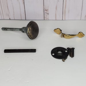 May include: A set of antique door hardware in gold and black. The set includes a door knob, a door handle, a strike plate, and screws.