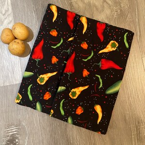 May include: Black fabric with a repeating pattern of red, orange, and yellow chilli peppers on a black background. The fabric is folded in half.