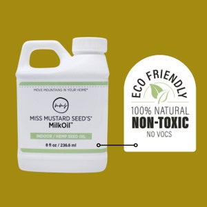 May include: A white plastic bottle of Miss Mustard Seed's MilkOil with a handle. The label includes the text "INDOOR / HEMP SEED OIL" and "8 fl oz / 236.6 ml". An "Eco Friendly" sticker is next to the bottle.