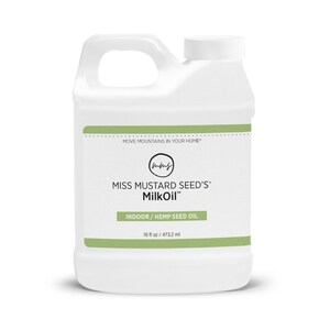 May include: A white plastic container of Miss Mustard Seed's MilkOil. The container has a handle and a white screw-on cap. The label includes the text "MOVE MOUNTAINS IN YOUR HOME", "INDOOR / HEMP SEED OIL", and "16 fl oz / 473.2 ml".