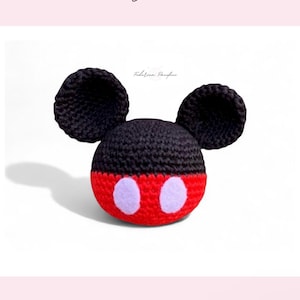 May include: A crocheted mouse head in black and red, with large black ears. The mouse has white oval accents on the red portion. The text "CHUBBY MOUSE" is above the mouse, and "Nivel de Habilidad: Principiante" is below.