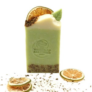 May include: A rectangular green soap bar with a white top, decorated with a dried orange slice and a green leaf. The soap has a logo that reads "The Washed-Up Bartender Soap". Dried orange slices and herbs are scattered around the soap.