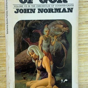 May include: Vintage paperback book cover for "Captive of Gor" by John Norman. The cover art depicts a woman in a dark purple outfit chained, with a warrior and a large bird in the background. The book is Volume VII in the Chronicles of Counter-Earth.