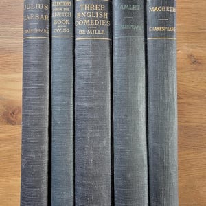 May include: A collection of five vintage books with dark blue covers. Titles include "Julius Caesar," "Selections from the Sketch Book," "Three English Comedies," "Hamlet," and "Macbeth." Gold lettering is visible on the spines.