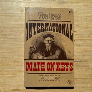 May include: Vintage book cover with the title "The Great International Math on Keys Book." The cover features a sepia-toned illustration of a man with a calculator and a globe. The book has a brown and red color scheme.