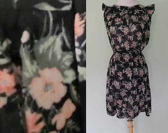 Könnte beinhalten: Ein schwarzes Minikleid mit rosa Blumenmuster, Rüschen am Ausschnitt und einer taillierten Passform. Das Kleid ist aus einem durchsichtigen Stoff.