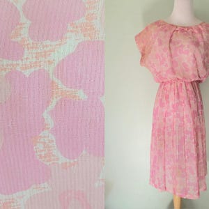 May include: A vintage pink dress with a floral design. The dress has a round neckline, short sleeves, and a pleated skirt. The fabric is delicate and semi-sheer. The dress is displayed on a mannequin.