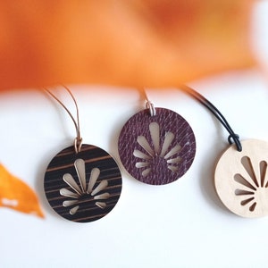 May include: Three wooden pendant necklaces with a fan-shaped cutout design. The pendants are in different colors: black and brown wood, dark purple leather, and natural wood.