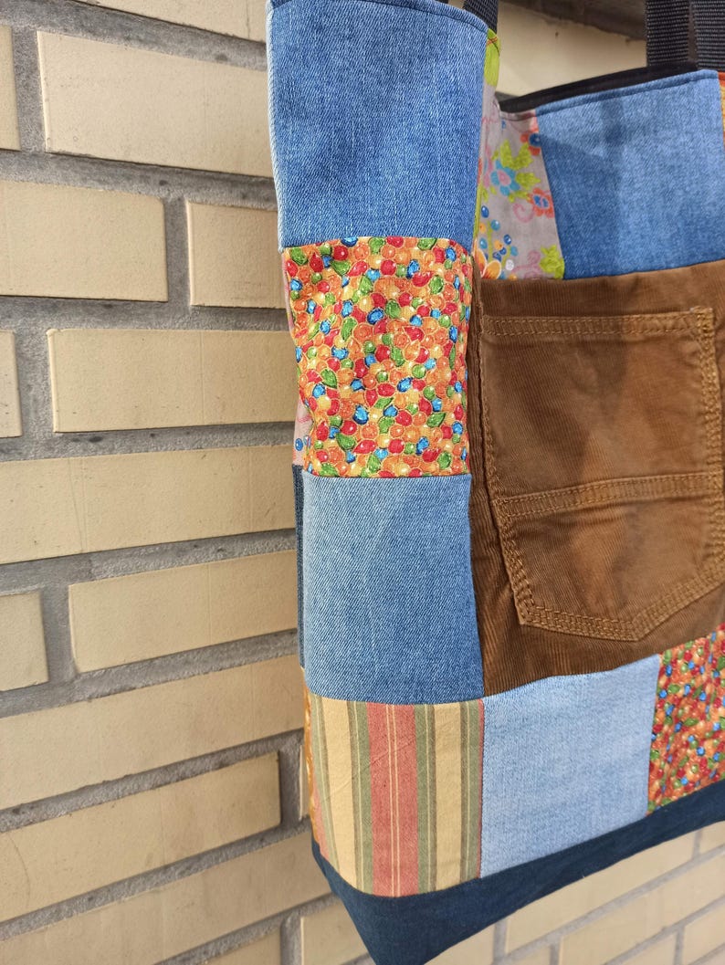 Pu&ograve; includere: Una borsa tote patchwork con denim, velluto a coste e tessuti fantasia. La borsa combina vari colori e trame, tra cui denim blu, velluto a coste marrone e motivi floreali e a righe. Una tasca &egrave; visibile sul davanti.