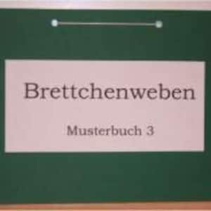 Könnte beinhalten: Eine grüne Tafel mit weißen Stecknadeln und einer weißen Schnur, die oben hängt. Die Tafel hat einen weißen Rahmen und den Text "Brettchenweben Musterbuch 3" in Schwarz.