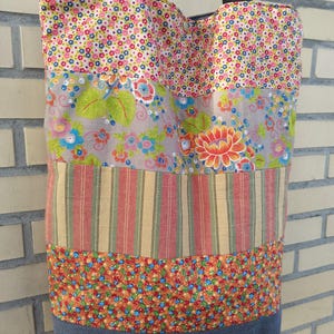 Könnte beinhalten: Eine Patchwork-Tragetasche mit Stoffbahnen mit Blumen- und Streifenmustern. Die Tasche hat einen Jeansstoff-Boden und schwarze Träger. Das farbenfrohe Design umfasst Rosa-, Blau-, Orange- und Grüntöne und schafft ein einzigartiges Accessoire.