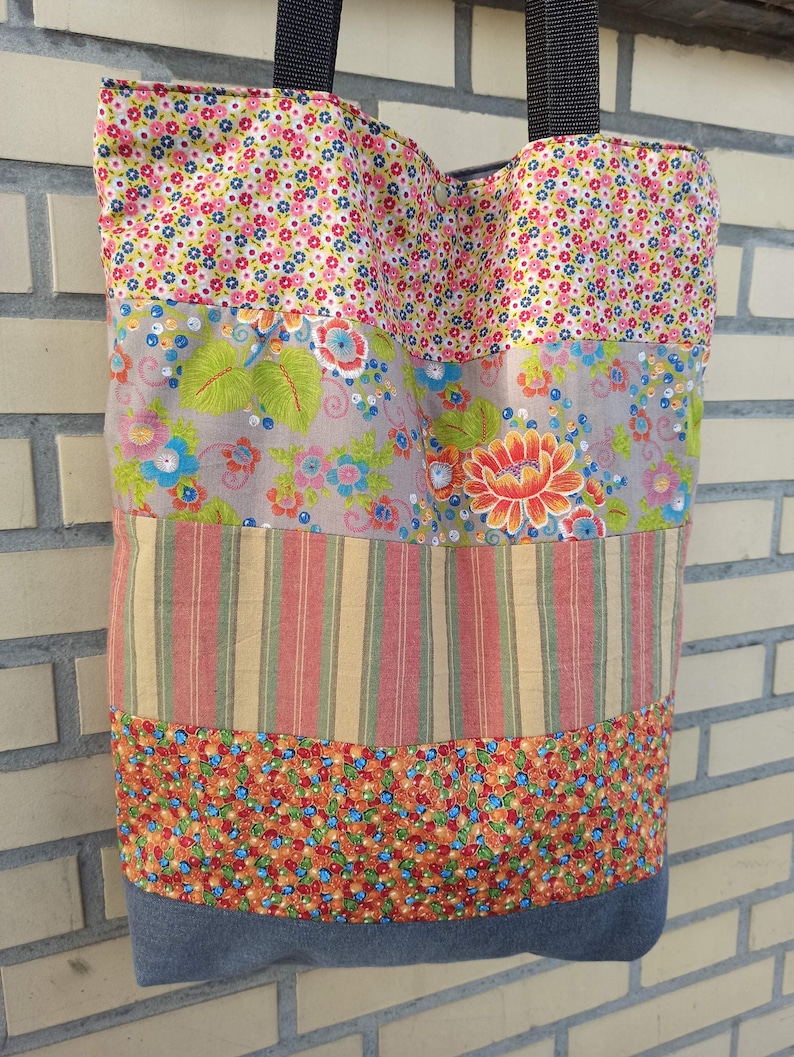 May include: A patchwork tote bag with a variety of floral and striped fabric panels. The bag features a denim base and black straps. The colorful design includes pink, blue, orange, and green hues, creating a vibrant and unique accessory.