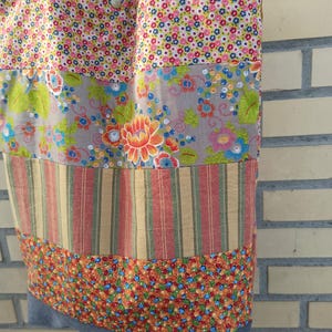 May include: A patchwork tote bag with a variety of floral and striped fabric panels. The bag features a denim base and black straps. The fabrics include pink, blue, orange, and green floral patterns, and red and yellow stripes.
