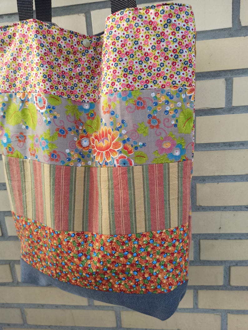 May include: A patchwork tote bag with a variety of floral and striped fabric panels. The bag features a denim base and black straps. The fabrics include pink, blue, orange, and green floral patterns, and red and yellow stripes.