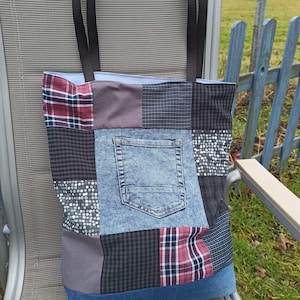 Könnte beinhalten: Eine Patchwork-Tragetasche mit einer Jeans-Tasche und schwarzen Griffen. Die Tasche weist eine Vielzahl von Stoffmustern auf, darunter Karos, Punkte und unifarbene Stoffe. Die Tasche steht auf einem Metallstuhl.