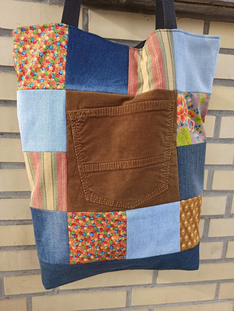 Pu&ograve; includere: Una borsa tote patchwork con una variet&agrave; di tessuti, tra cui denim, velluto a coste e cotone fantasia. La borsa presenta un'ampia tasca in velluto a coste marrone e una tracolla nera. Il design patchwork incorpora tessuti blu, marroni e fantasia.