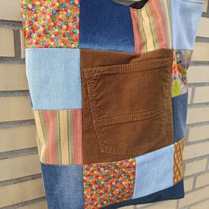 Pu&ograve; includere: Una borsa tote patchwork con una variet&agrave; di tessuti, tra cui denim, stampe floreali e velluto a coste. La borsa presenta un'ampia tasca in velluto a coste marrone e manici neri. La borsa &egrave; un mix di blu, marrone, arancione e azzurro.