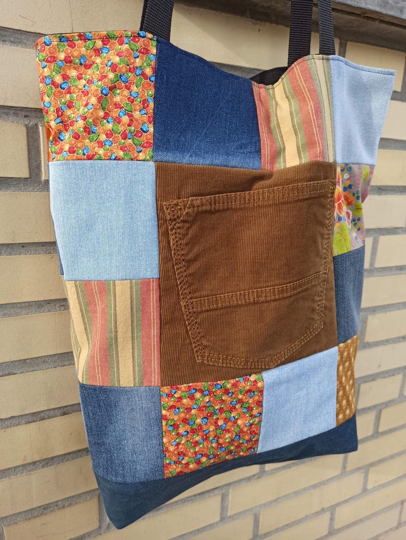 Pu&ograve; includere: Una borsa tote patchwork con una variet&agrave; di tessuti, tra cui denim, stampe floreali e velluto a coste. La borsa presenta un'ampia tasca in velluto a coste marrone e manici neri. La borsa &egrave; un mix di blu, marrone, arancione e azzurro.