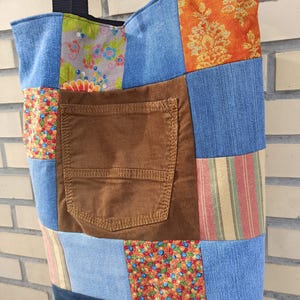 Pu&ograve; includere: Borsa tote patchwork con una variet&agrave; di tessuti, tra cui denim, stampe floreali e velluto a coste. La borsa presenta una tasca in velluto a coste marrone e cinghie nere. Il design incorpora vari colori e motivi, creando un aspetto unico e artigianale.