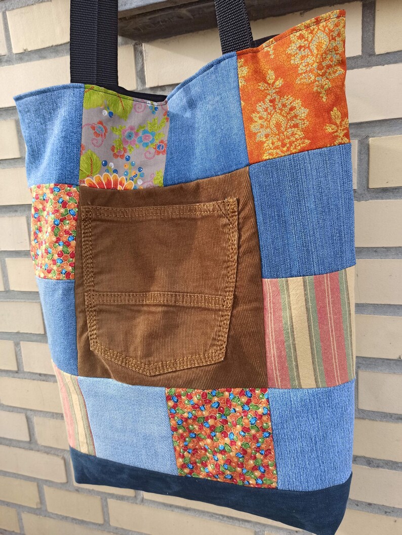 Pu&ograve; includere: Borsa tote patchwork con una variet&agrave; di tessuti, tra cui denim, stampe floreali e velluto a coste. La borsa presenta una tasca in velluto a coste marrone e cinghie nere. Il design incorpora vari colori e motivi, creando un aspetto unico e artigianale.