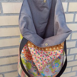 May include: Open tote bag with a floral pattern and a gray interior. The bag has a black strap and a brown accent. The exterior features a mix of floral and striped fabrics, with a snap closure at the top.