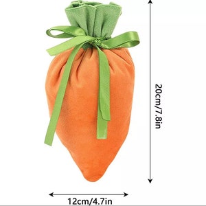 May include: A carrot-shaped drawstring bag made of orange velvet with green velvet leaves at the top. The bag is tied with a green ribbon. The bag measures 20cm/7.8in tall and 12cm/4.7in wide.