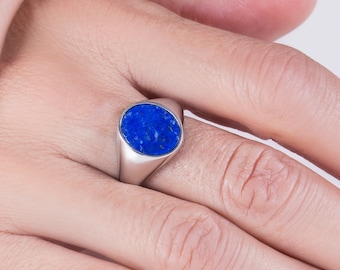 Op de afbeelding: Een zilveren ring met een blauwe ovale lapis lazuli-edelsteen. De ring wordt gedragen aan een vinger.