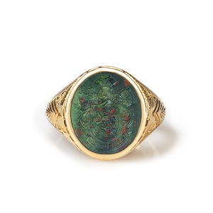 Peut inclure: Une bague en or avec une pierre ovale verte orn&eacute;e d'un blason grav&eacute; d&eacute;taill&eacute;. La pierre est de couleur rouge et verte.