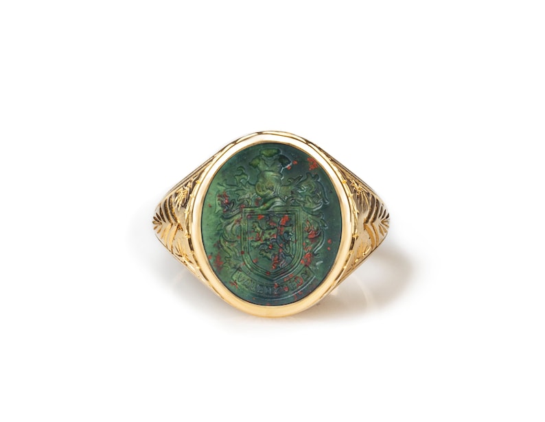 Peut inclure: Une bague en or avec une pierre ovale verte orn&eacute;e d'un blason grav&eacute; d&eacute;taill&eacute;. La pierre est de couleur rouge et verte.