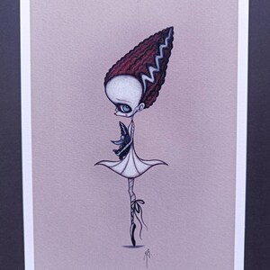 May include: A black and white illustration of a Frankenstein-inspired ballerina holding a small black bird. The ballerina is wearing a white dress and black shoes. The background is a light pink color.