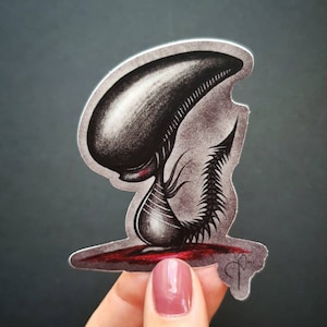 Puede incluir: Una pegatina en blanco y negro de un extraterrestre de dibujos animados con fondo rojo. El extraterrestre está en posición de cuclillas con la cabeza inclinada.