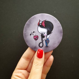 May include: A round mirror with a white background and a cartoon illustration of Snow White with a red apple and a syringe. The illustration is in a dark, gothic style.