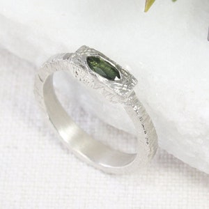 May include: A silver ring with a textured band and a green gemstone set in the center.