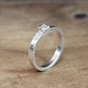 May include: A silver ring with a hammered texture and a small, square-shaped gemstone set in the top.