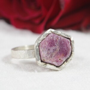 May include: A silver ring with a pink ruby gemstone set in a hexagonal bezel. The ring has a hammered texture.