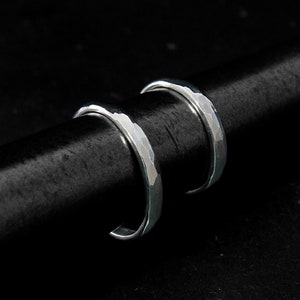 May include: Two silver hammered metal rings, stacked on top of each other, on a black surface.