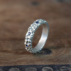 May include: A silver band ring with a textured surface and four small blue gemstones.