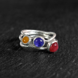 May include: A silver ring with three stones: a red stone, a blue stone, and an orange stone.