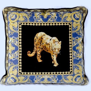 May include: A decorative throw pillow with a blue and gold patterned border. The center of the pillow features a black background with a gold and brown leopard print design.