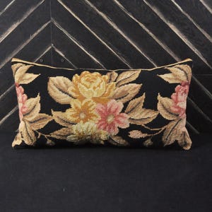 Peut inclure: Un coussin rectangulaire noir avec un motif floral. Les fleurs sont jaunes, roses et brunes. Le coussin est sur un fond noir à motif chevron.