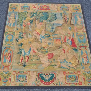 May include: A colorful tapestry depicting a scene of people gathering fruit in a garden. The tapestry is framed with a decorative border featuring cherubs and floral motifs.