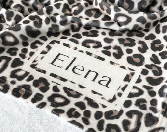 May include: A white and brown leopard print throw blanket with the name "Elena" printed in a white rectangle.