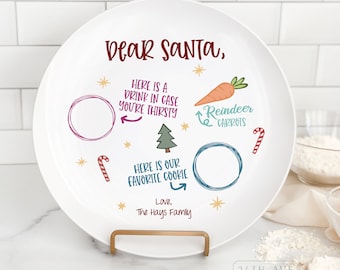 May include: White ceramic plate with a festive design for Santa. It says "Dear Santa" and includes spaces for a drink, cookies, and reindeer carrots. The text reads "Here is a drink in case you're thirsty", "Here is our favorite cookie", and "Reindeer Carrots".