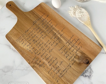 May include: A wooden cutting board with a handwritten recipe for "Cookies in a Jar" engraved on the surface. The recipe includes ingredients such as butter, sugar, flour, and spices. The board has a handle and is perfect for serving or displaying in the kitchen.